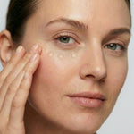 Woman gently applying freezeframe REVITALEYES eye gel cream beneath her eye, with three small drops of product visible on the under-eye area to target wrinkles, puffiness and dark circles.